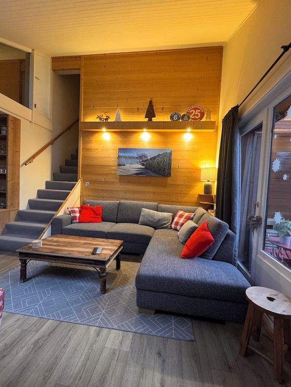 A modern living room with a grey sectional sofa, a wooden coffee table, and a staircase leading to an upper floor.