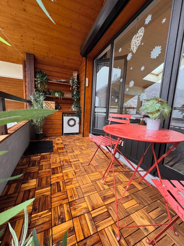 A wooden deck with a herringbone floor pattern, a red metal table and chairs, and potted plants. - Spacious, family 3 bedroom duplex - only 50m from the ski slopes (Saint-Jean-D'aulps)
