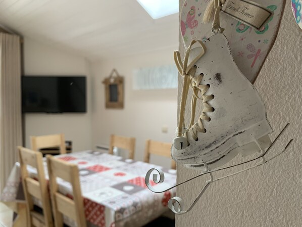 Une pièce comprenant une table à manger, des chaises, un téléviseur et un mur décoré de chaussures.