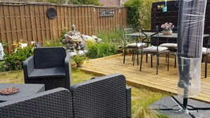 Un patio con mobiliario de mimbre, una terraza de madera y un elemento decorativo de rocas.
