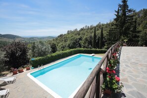 A rectangular swimming pool with a wooden deck and a stone pathway.