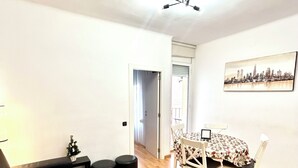 A living room with a dark sofa, a small table with chairs, a ceiling fan, and a cityscape painting on the wall. - Parking available. Pets accepted. Subway nearby. Near the Sagrada Familia (Barcelona)