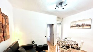 A living room with a sofa, a small table with a laptop, a dining table with chairs, and a cityscape painting on the wall. - Parking available. Pets accepted. Subway nearby. Near the Sagrada Familia (Barcelona)