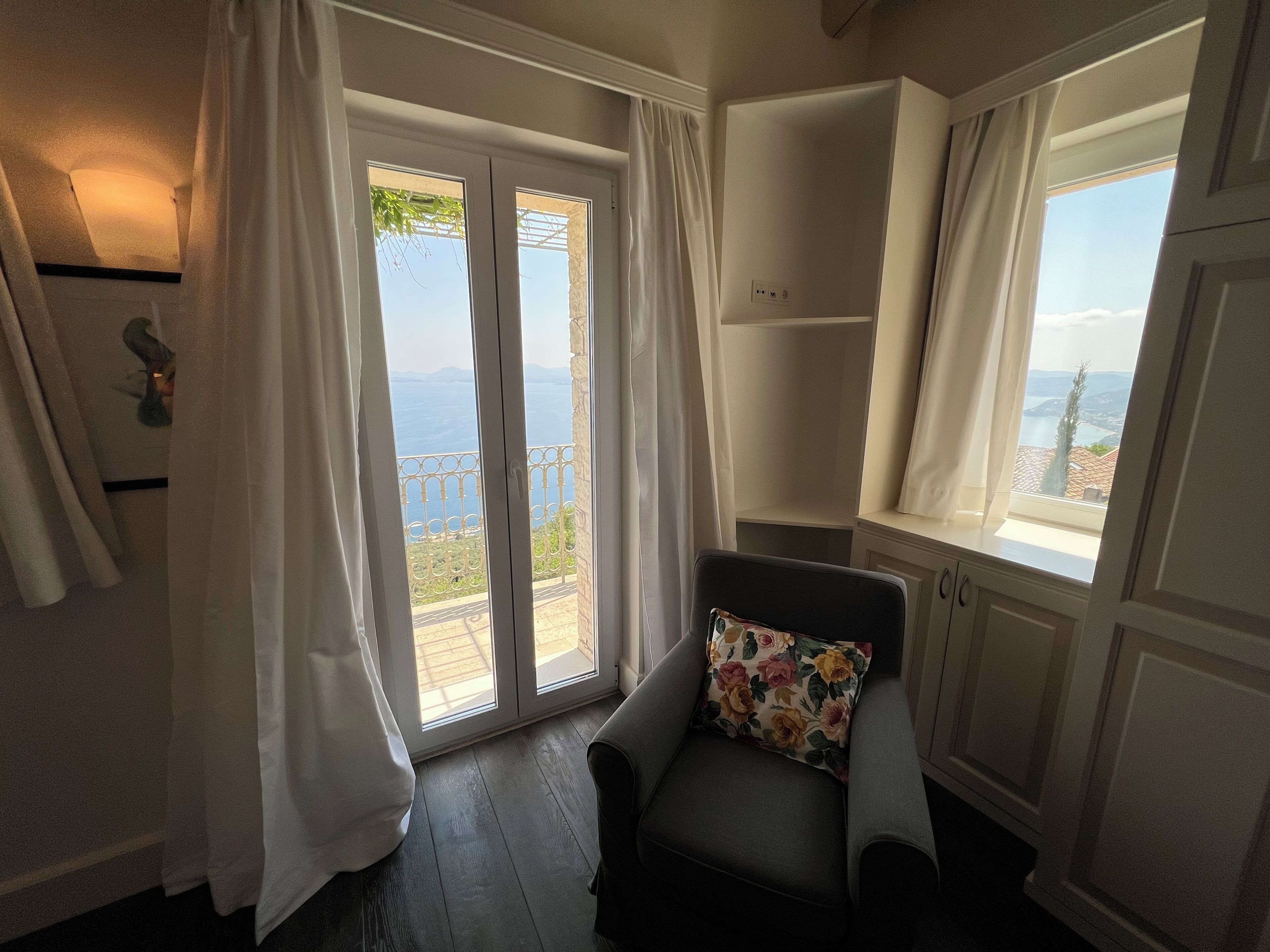 A room with a balcony, a chair with a floral pillow, and a view of the sea.
