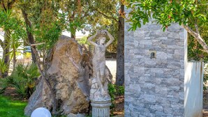 Un jardín con un muro de piedra, una roca grande y una estatua.