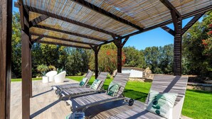 Un área de estar al aire libre cubierta, con sillones reclinables y una cesta de mimbre.