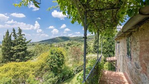 Ein Steinhaus mit Balkon, das einen üppigen Landschaftsbereich mit Bäumen und Hügeln blickt.