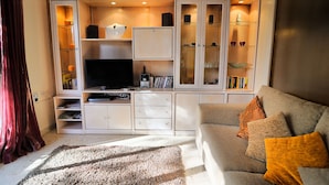 Un salón con sofá, televisión y estanterías empotradas con libros y objetos decorativos.