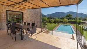 A covered patio with a stone wall, a pool, and a view of mountains. - CAN SIVELLA GROC - Lovely mediterranean villa with mountain views & stylish pool (Sóller)