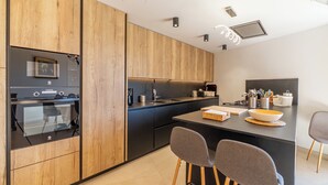 A modern kitchen with wooden cabinets, a black countertop, and a central island with bar stools. - CAN SIVELLA GROC - Lovely mediterranean villa with mountain views & stylish pool (Sóller)