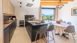 A modern kitchen with a central island, dining table with chairs, and a view of the outdoors. - CAN SIVELLA GROC - Lovely mediterranean villa with mountain views & stylish pool (Sóller)