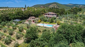 Una villa con piscina rodeada de exuberante vegetación y colinas al fondo.