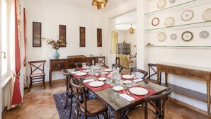 Un espace repas avec une longue table dressée pour six personnes, entourée de chaises en bois.