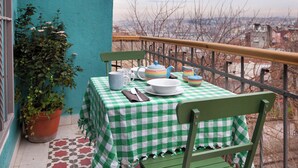 Ein Balkon mit kariertem Tischleinentuch, einer Topfpflanze und Geschirr.