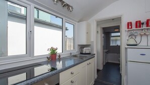 A modern kitchen with white cabinets, a granite countertop, and a window providing natural light. - Seashell Cottage - 50 meters from the beach (Walmer)