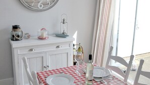 A dining area with a checkered tablecloth, white chairs, a white cabinet with decorative items, and a view through a window. - Seashell Cottage - 50 meters from the beach (Walmer)