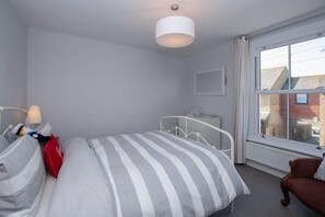 Ett sovrum med en säng, ett nattduksbord, en lampa och ett fönster med utsikt över byggnader.