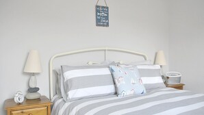 A neatly arranged bedroom with a bed, bedside tables, a nightstand, a lamp, and a small clock. - Seashell Cottage - 50 meters from the beach (Walmer)