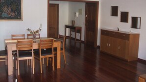 A dining area with a wooden table and chairs, a cabinet, and a painting on the wall. - Large three bedroom by the seaside promenade (Funchal)