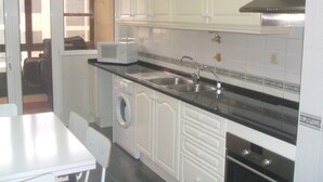A compact kitchen with white cabinets, a microwave, a sink, a washing machine, and an oven. - Large three bedroom by the seaside promenade (Funchal)