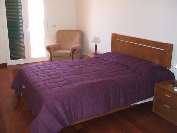Een slaapkamer met een bed, een stoel, een nachtkastje en een lamp.