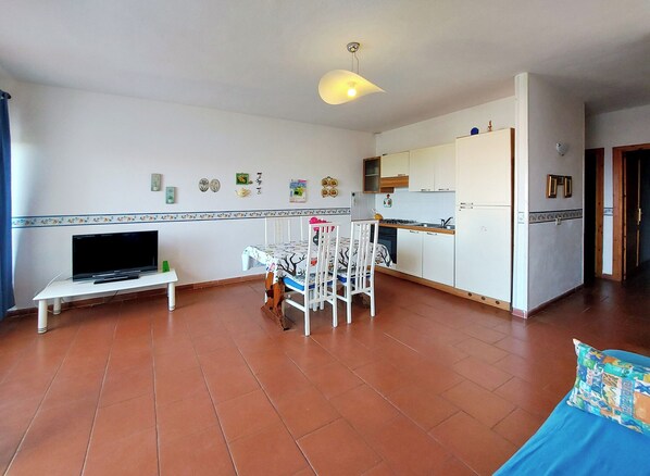 A compact living space with a TV, dining table, chairs, kitchen area, and a sofa.