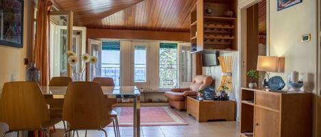 Amplia sala de estar con techo de madera, una mesa de comedor con sillas, un sofá y un televisor instalado en la pared.