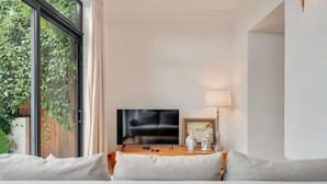 A modern living room with a large window, a flat-screen TV, a wooden side table, and a sofa. - Rochinha’s house with fabulous views over the bay of funchal (Funchal)