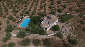 Vista aérea de una propiedad con piscina, un edificio blanco de techo con tejas y un jardín cercado.