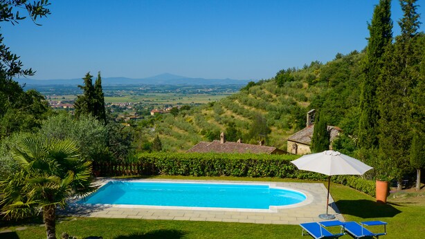 A swimming pool with a view of a hilly landscape, a lawn, and a few lounge chairs.
