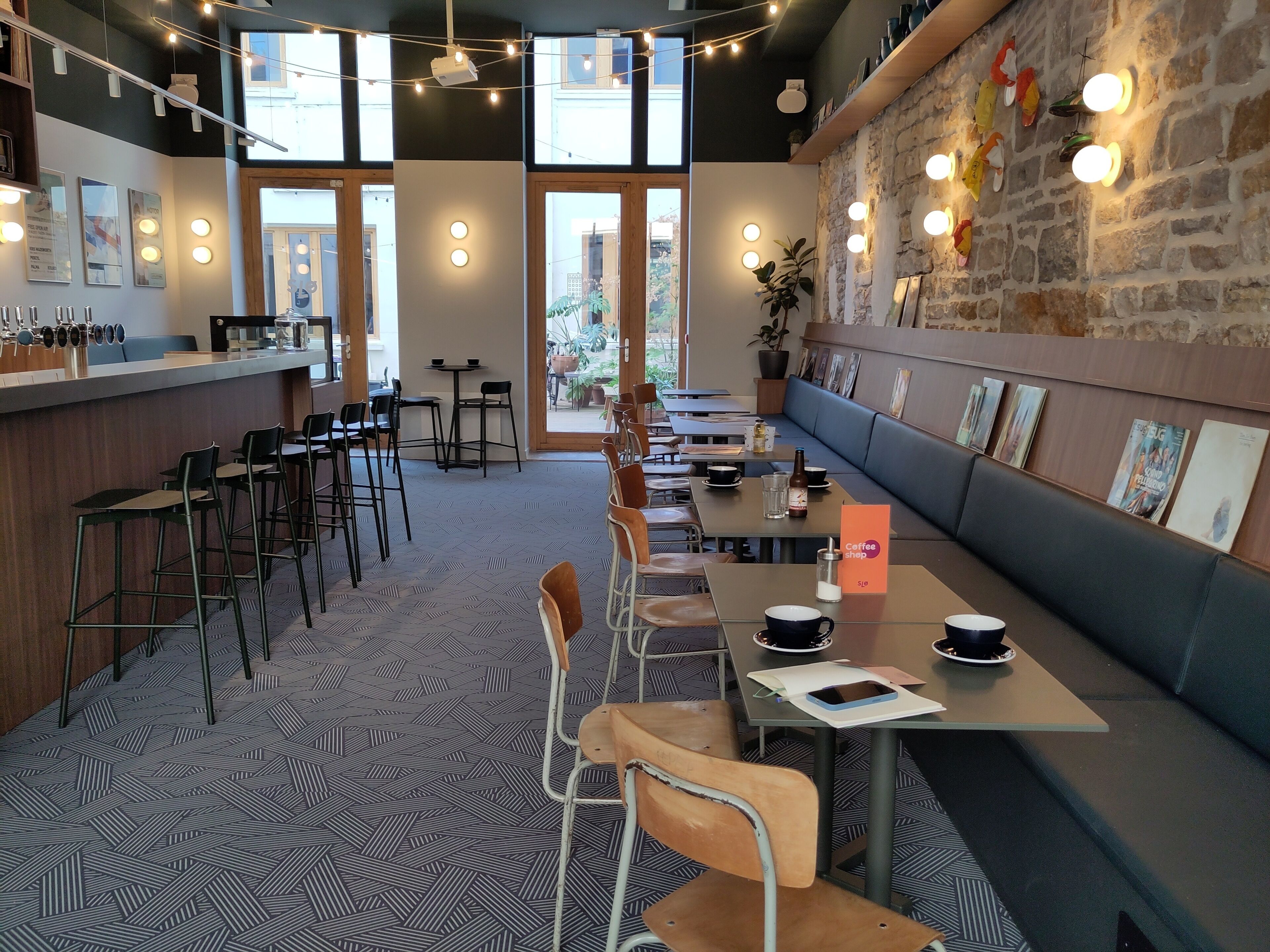Un café moderno con barra, asientos y una pared de piedra decorada con obras de arte.