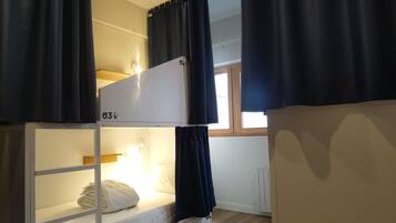 Una cama litera con cabecera blanca, ventilador de techo y ventana con cortinas.