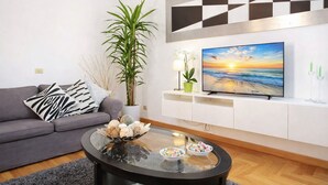 A modern living room with a grey sofa, a glass coffee table with decorative items, a large flat-screen TV on a white entertainment unit, and a large potted plant. - Lux comfort privacy in the center of Rome, shared by a group of 10 friends (Roma)