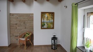 A room with a stone wall, a wicker chair, a painting, a lantern, and a green curtain. - Enjoy the tranquility of nature, - / juniper reserve in Alendorf (Blankenheim /Alendorf)