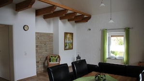 A dining area with a wooden table, black chairs, a green tablecloth, a clock, a painting, and a window with green curtains. - Enjoy the tranquility of nature, - / juniper reserve in Alendorf (Blankenheim /Alendorf)
