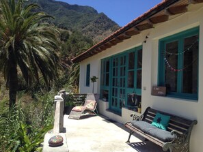 A building with a white exterior and teal windows, a bench, and a palm tree in the foreground. - CASA AURA sunshine over the sea (Hermigua la gomera)