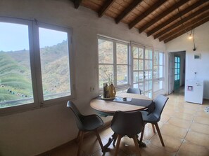 A dining area with a table and chairs, large windows with a view of the countryside, and a wooden ceiling. - CASA AURA sunshine over the sea (Hermigua la gomera)