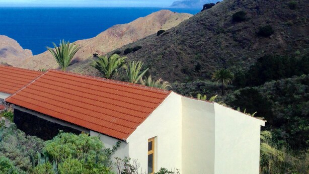 A coastal building with a red roof, surrounded by greenery and hills. - CASA AURA sunshine over the sea (Hermigua la gomera)