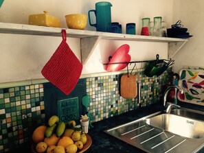 A kitchen with a tiled backsplash, a fruit bowl, a sink, and various kitchen utensils and containers on shelves. - CASA AURA sunshine over the sea (Hermigua la gomera)