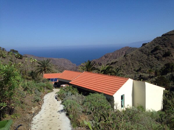 A small building with a red roof, surrounded by greenery and a rocky hillside.