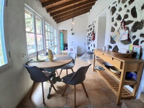 A dining area with a wooden table and chairs, a stone wall with decorations, and a view through large windows. - CASA AURA sunshine over the sea (Hermigua la gomera)