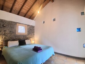 A bedroom with a stone wall, a bed with a blue bedspread, and a window. - CASA AURA sunshine over the sea (Hermigua la gomera)