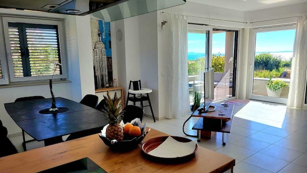 Une cuisine moderne avec un coin repas, de grandes fenêtres et une vue sur l’extérieur.