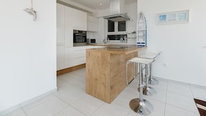 Une cuisine moderne avec des meubles blancs, un îlot central en bois, des appareils électroménagers en acier inoxydable et un tabouret de bar.