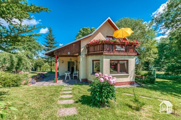 Una casa de dos pisos con balcón, terraza de madera y jardín.
