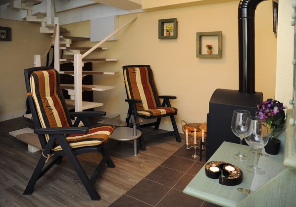 A modern living room with a staircase, two striped armchairs, a small table with candles and glasses, and a fireplace.