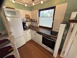 A compact kitchen with white cabinets, a built-in oven, a microwave, and a window with blinds.