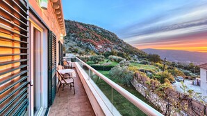 Un balcon donnant sur une colline et offrant une vue sur le coucher de soleil.