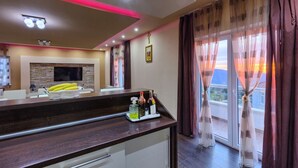 Une cuisine moderne avec un plan de travail foncé, un téléviseur à écran plat et un coin repas offrant une vue sur le coucher de soleil.