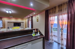 Una cocina moderna con encimera oscura, televisor de pantalla plana y comedor con vistas al atardecer.